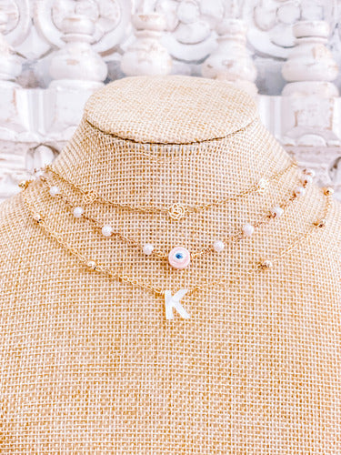 gold plated chain necklace with gold plated roses on the first necklace, the second necklace is faux pearls on a gold plated chain with a pink evil eye and the 3rd necklace is a gold plated chain with little balls and an initial charm