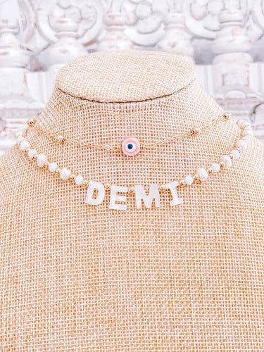 pearl necklace with name and a gold plated necklace choker with a pink evil eye charm